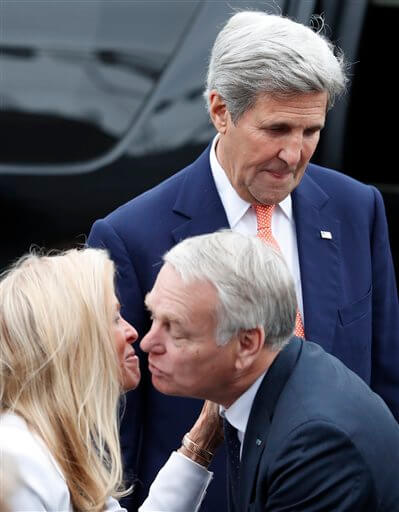 U.S Secretary of State John Kerry, top, looks down as French Foreign Minister Jean-Marc Ayrault kisses U.S ambassador to France Jane Hartley  on the Champs Elysees avenue before the Bastille Day Parade in Paris, Thursday, July 14, 2016. (AP Photo/Francois Mori)